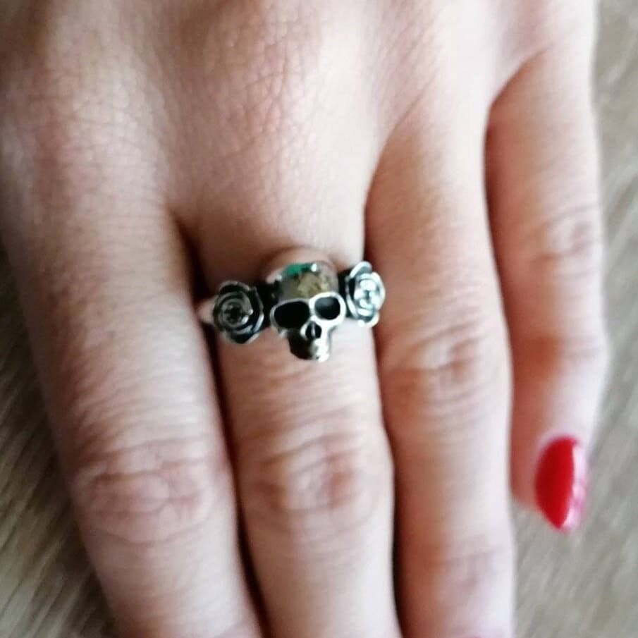 May include: A silver skull ring with three small silver roses on each side of the skull